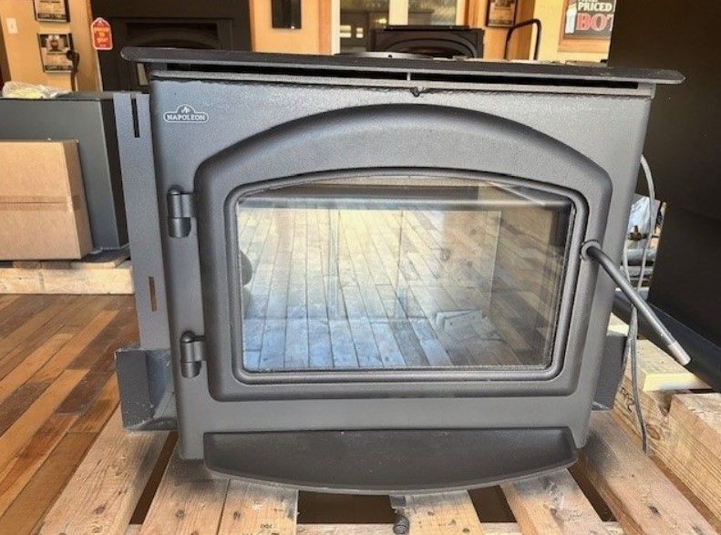 Black wood-burning stove with glass door on a wooden floor indoors.