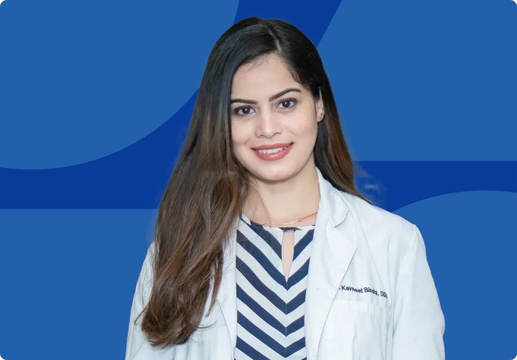Dr. Kavneet Bindra wearing a white monogrammed lab coat and standing in front of a blue background