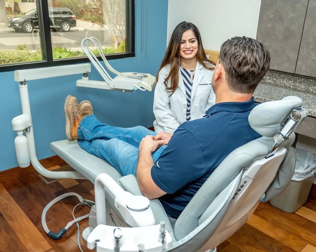 A male patient is seated in a dental chair while talking with Dr. Kavneet Bindra