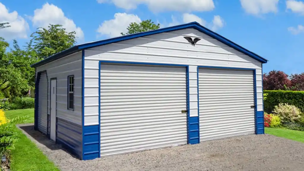 Blue and white metal two-car garage with roll-up doors, set against a blue sky with trees and grass.