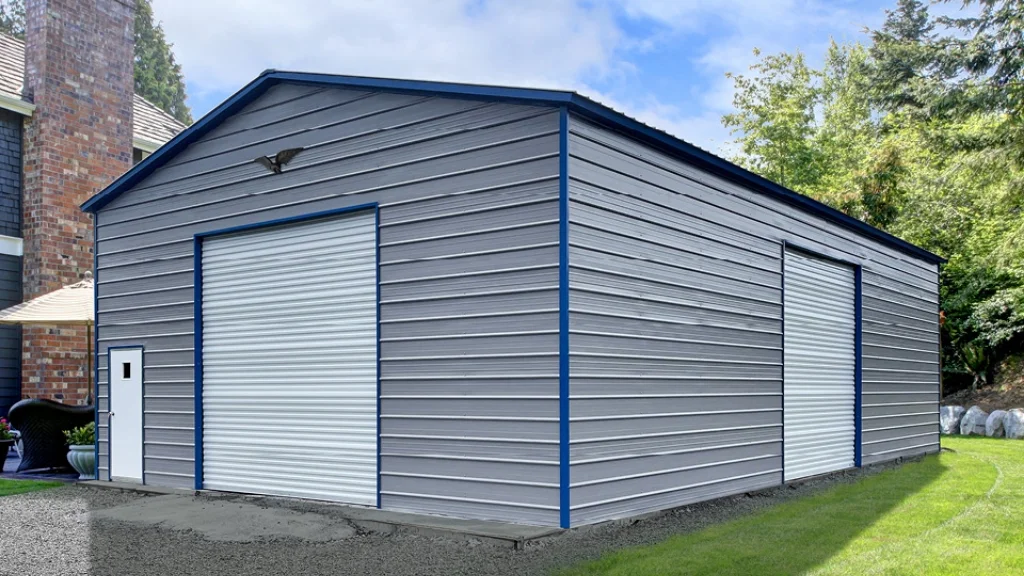 Gray metal garage with two roll-up doors and a pedestrian door, set on a grassy lawn with a brick chimney.