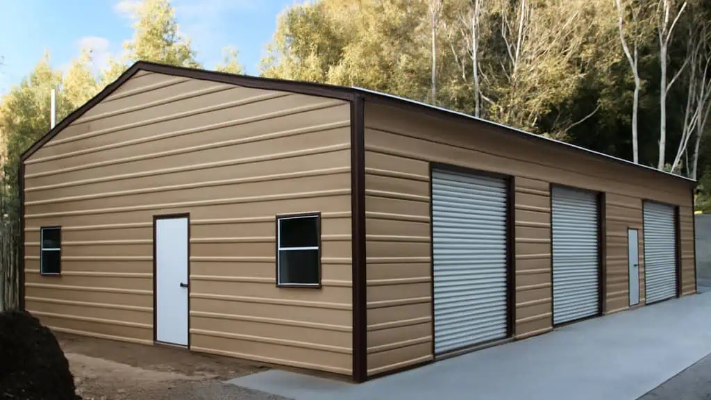 Tan metal garage with three garage doors and a side entry door, set against a wooded backdrop.