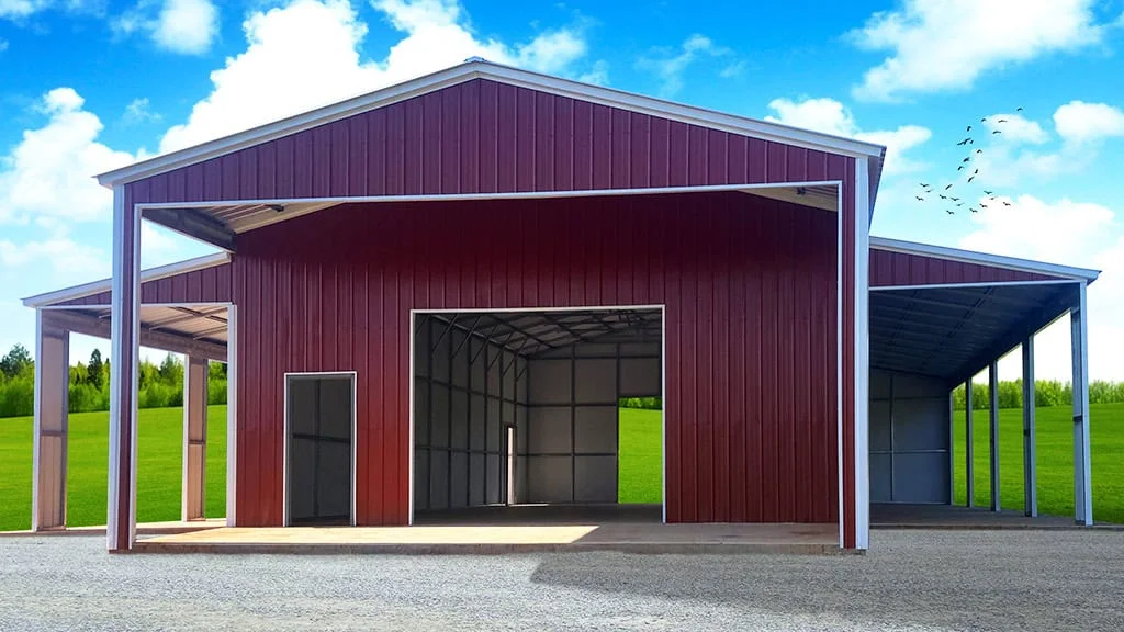 Red metal barn with open bays and attached lean-to, set on a grassy area under a blue sky.