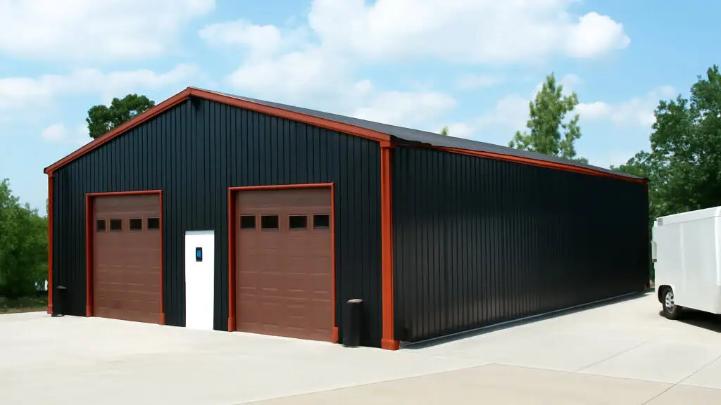 Black metal building with brown garage doors and trim, set on concrete, blue sky.