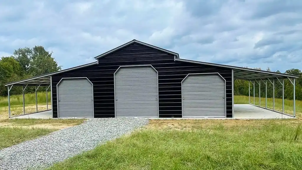 Black barn with three large doors, silver-covered awnings, and a gravel path in a grassy field.