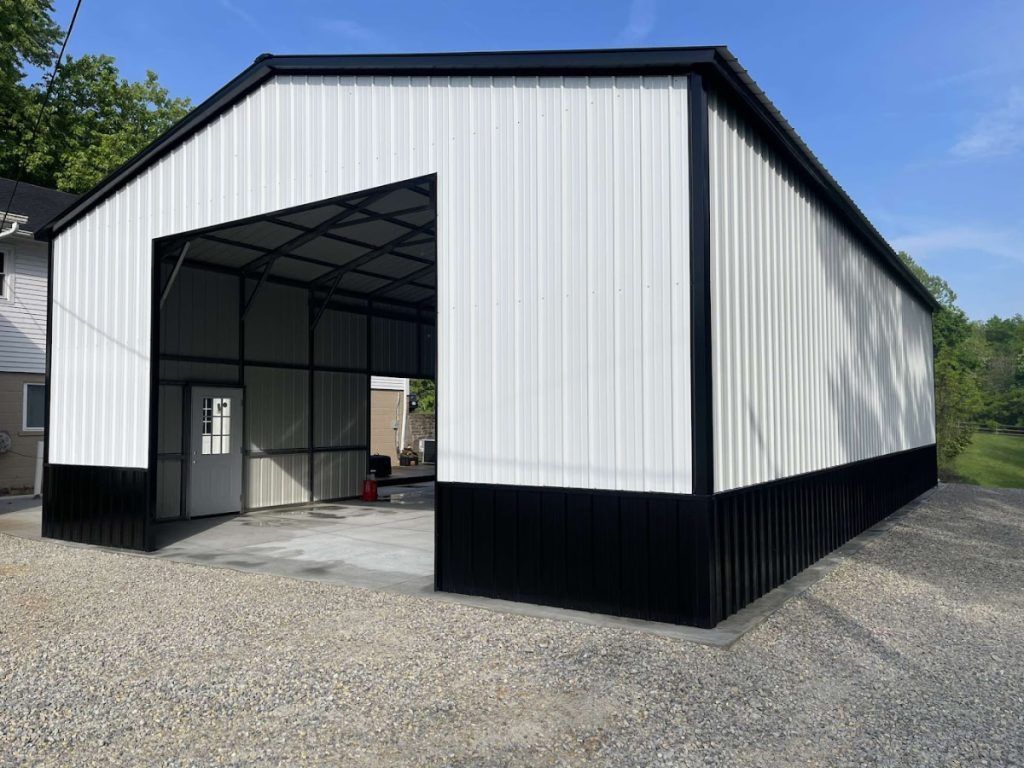 Black and white metal barn with open front, on gravel.