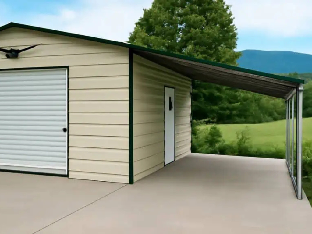 Tan metal garage with green trim, carport, and a concrete pad, set in a green field, mountain in background.