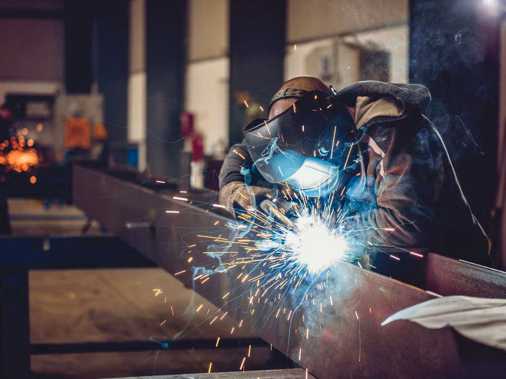 Welder in a workshop, using a welding torch. Sparks and bright light emanate from the weld.