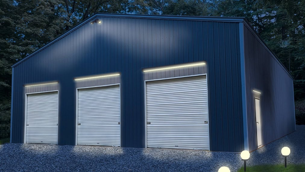 Red metal barn with open bays and attached lean-to, set on a grassy area under a blue sky.