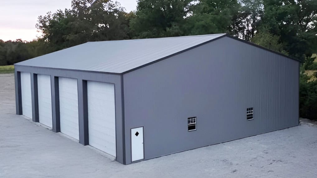 Dark blue metal garage with three bays, illuminated overhead and by small lights on a gravel ground.