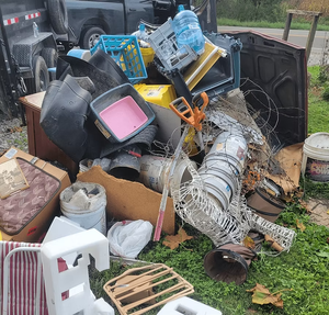Pile of trash including various objects on grass with truck and trailer.