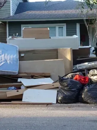 Pile of water-damaged furniture and trash bags piled on the side of a street in front of a house.
