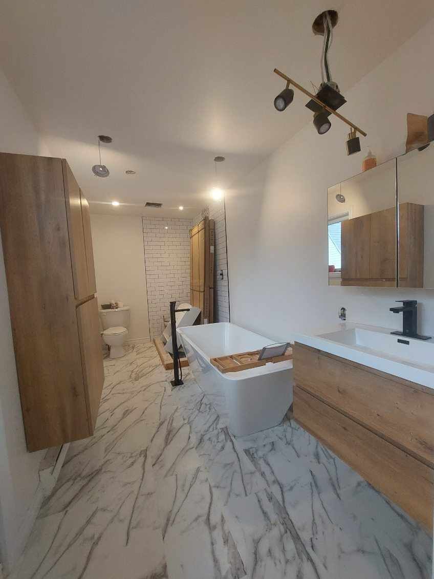 Salle de bains moderne avec sol en marbre, meubles en bois, baignoire et éclairage sur rail.