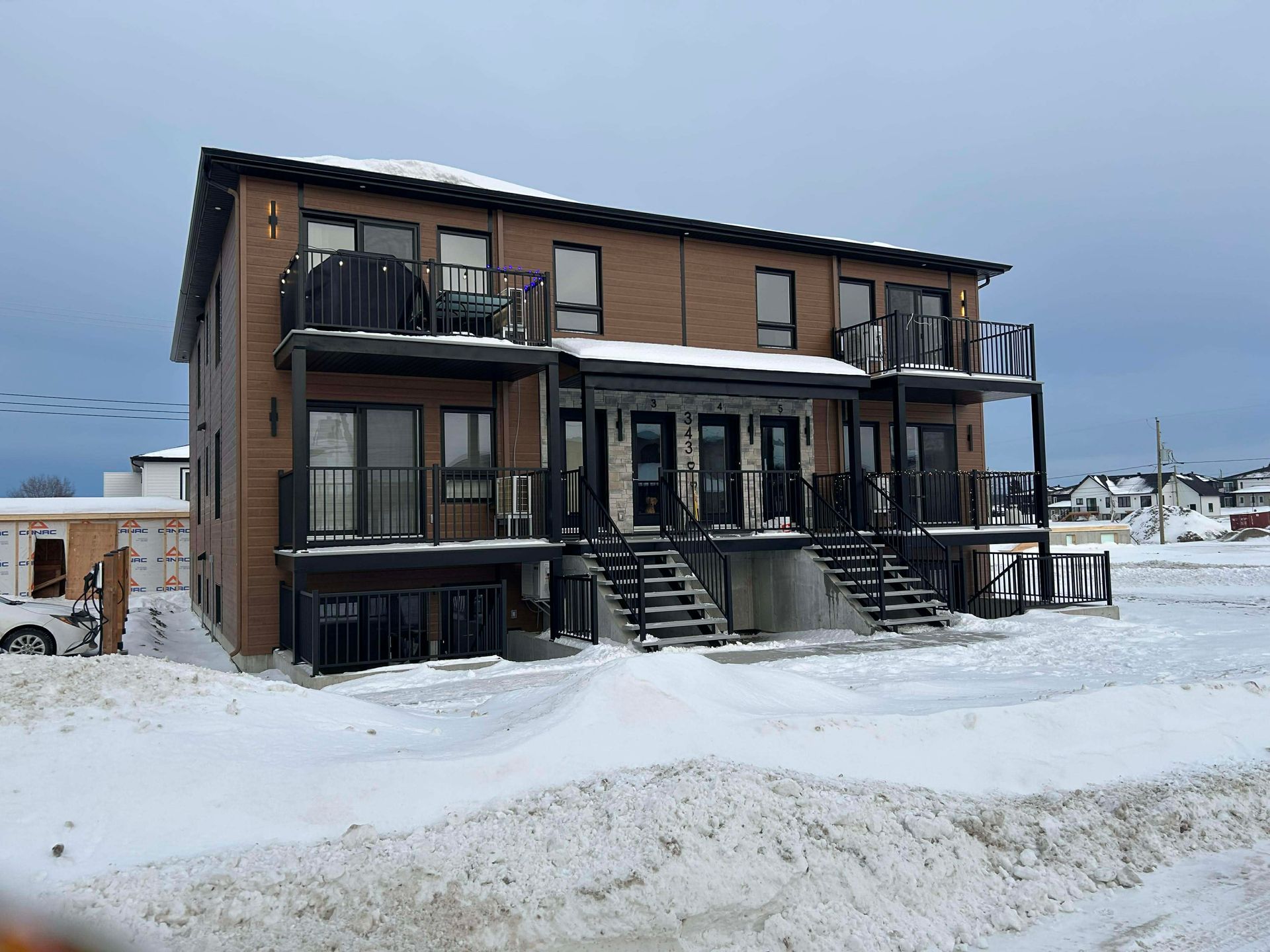 Immeuble de deux étages en briques, avec balcons et escaliers noirs, recouvert de neige ; ciel couvert.