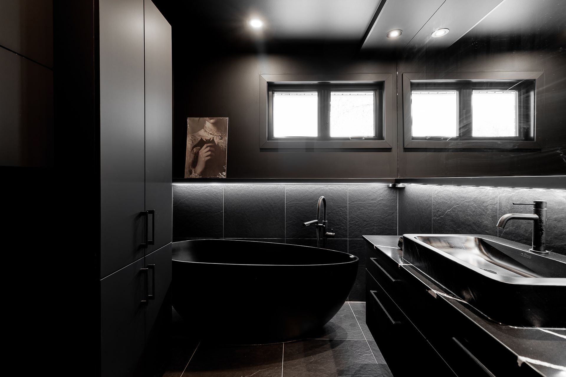 Salle de bains moderne noire avec baignoire, meuble-lavabo et rangements.