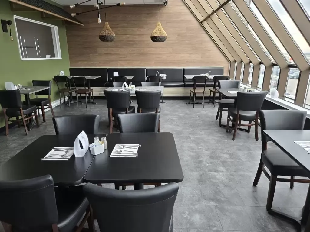 Intérieur de restaurant avec tables, chaises et banquettes noires près des fenêtres, panneaux muraux en bois
