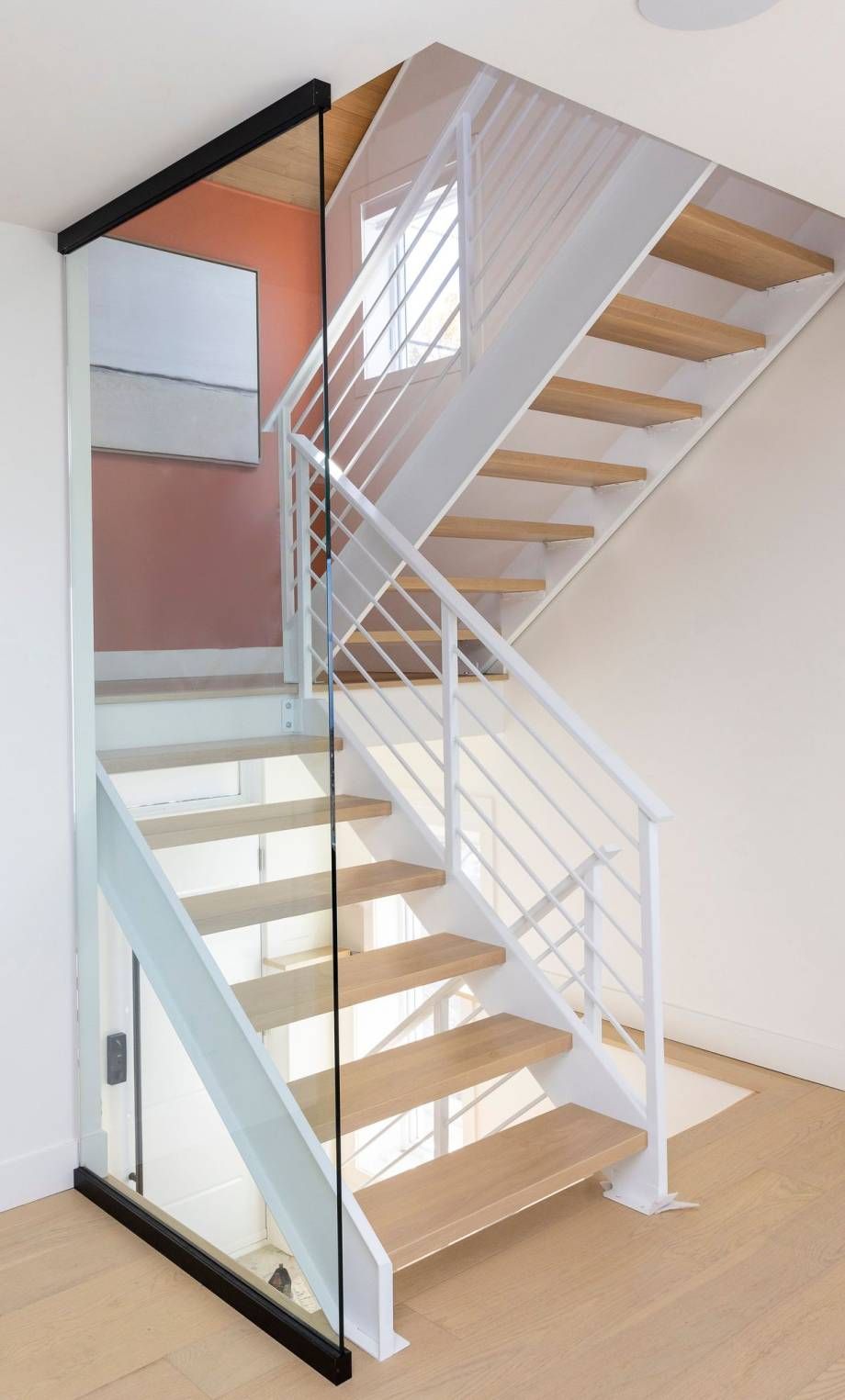 Escalier blanc avec paroi de verre, marches en bois et rampes en métal dans une maison moderne.