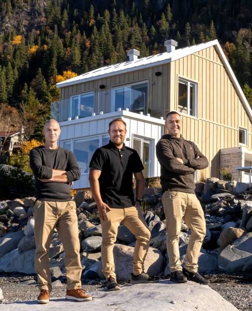 Trois hommes se tiennent devant une maison moderne, les bras croisés. Montagnes et eau en arrière-plan.
