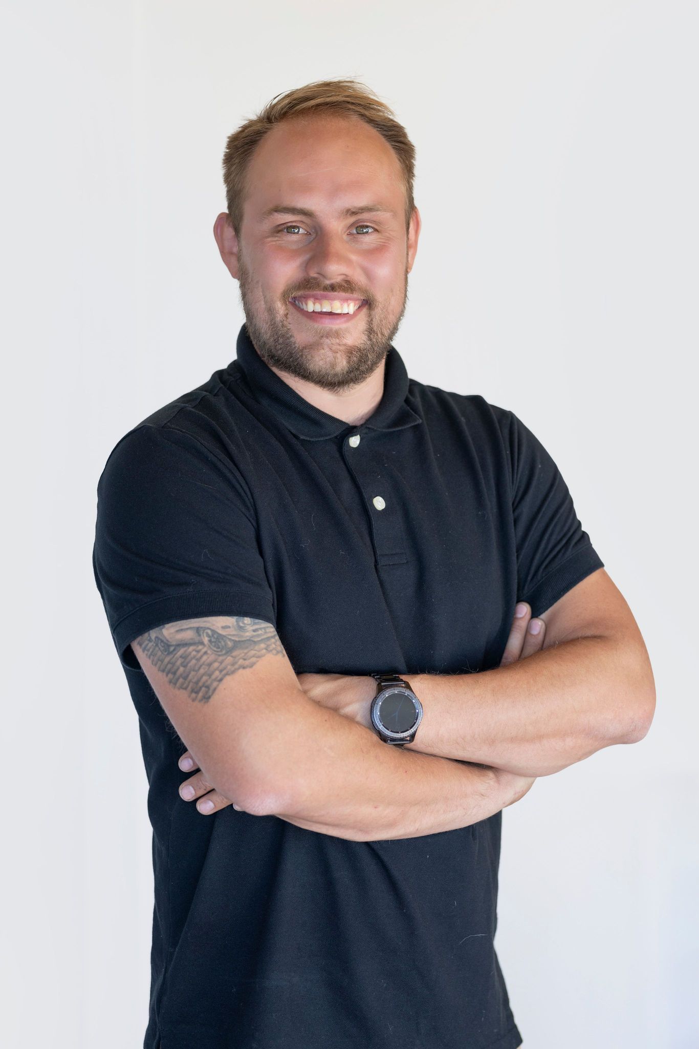 Homme aux bras croisés, vêtu d'une chemise noire, souriant à l'objectif.