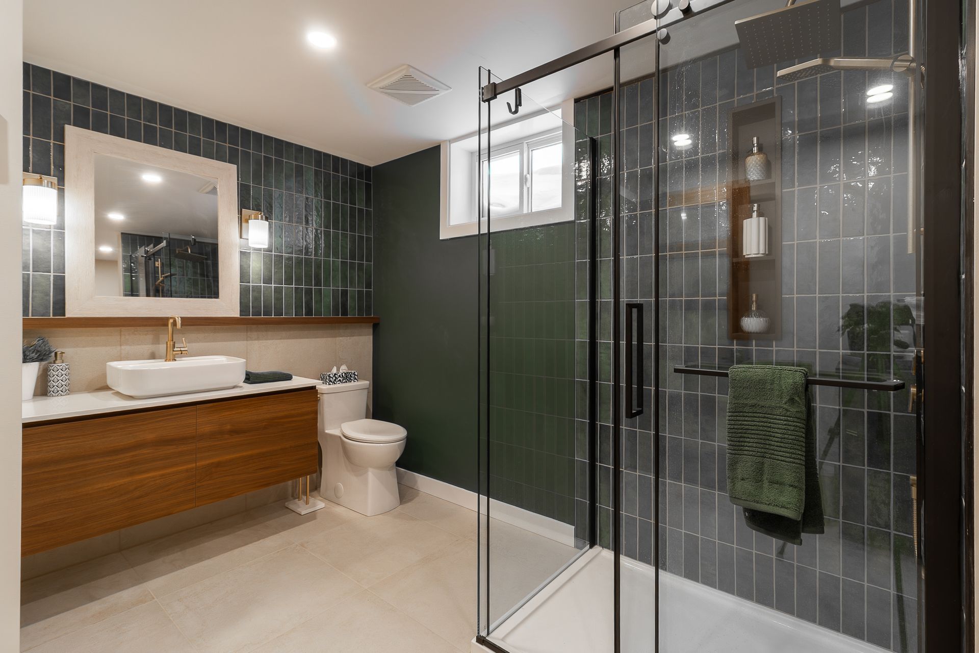 Salle de bains moderne avec carrelage bleu sarcelle foncé, douche en verre, meuble-lavabo en bois et robinetterie dorée.