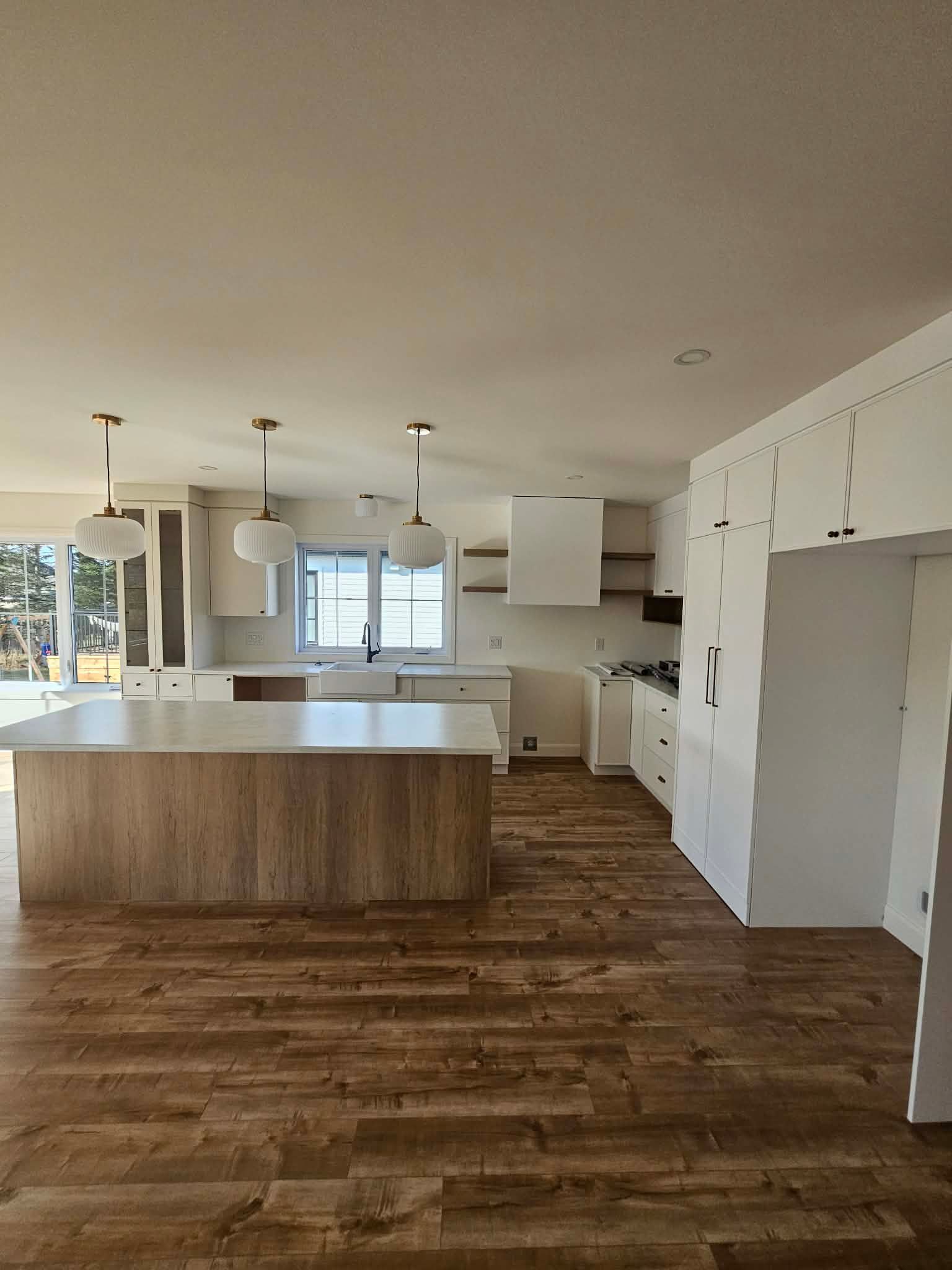 Cuisine spacieuse avec sol imitation bois, placards blancs et un grand îlot central avec un plan de travail clair.