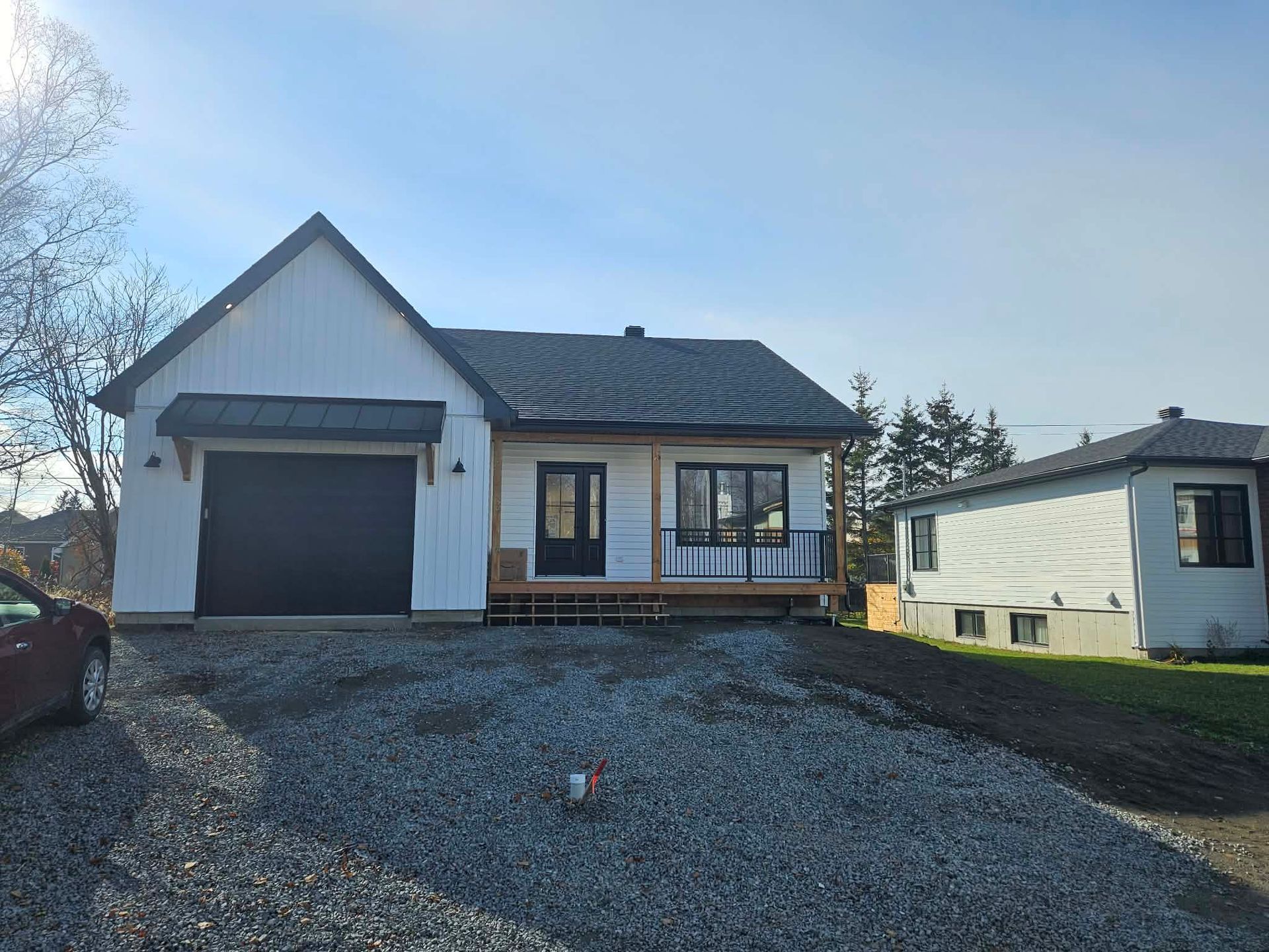 Maison blanche neuve avec porte de garage noire, porche et allée de gravier.