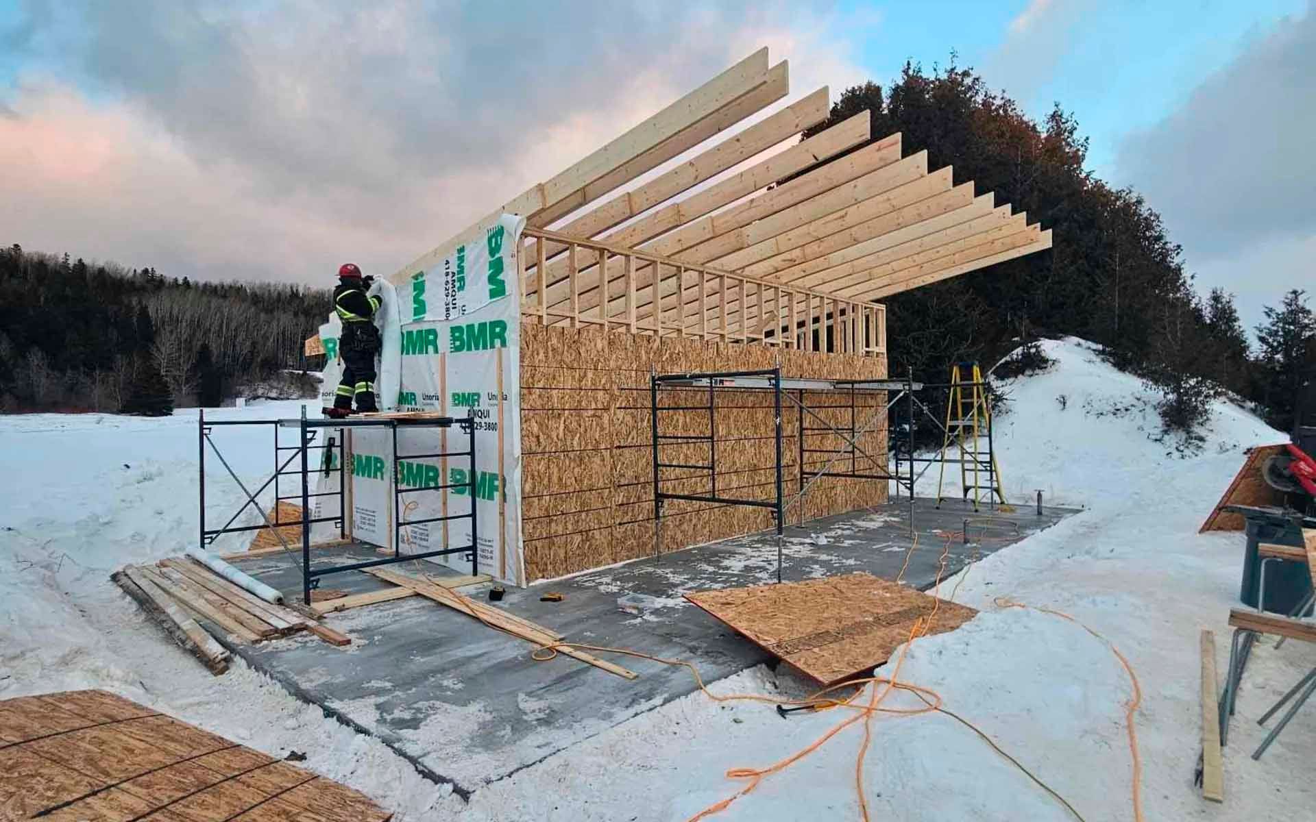 Construction d'un bâtiment en hiver : ossature bois avec revêtement en OSB, échafaudage, un ouvrier et neige.
