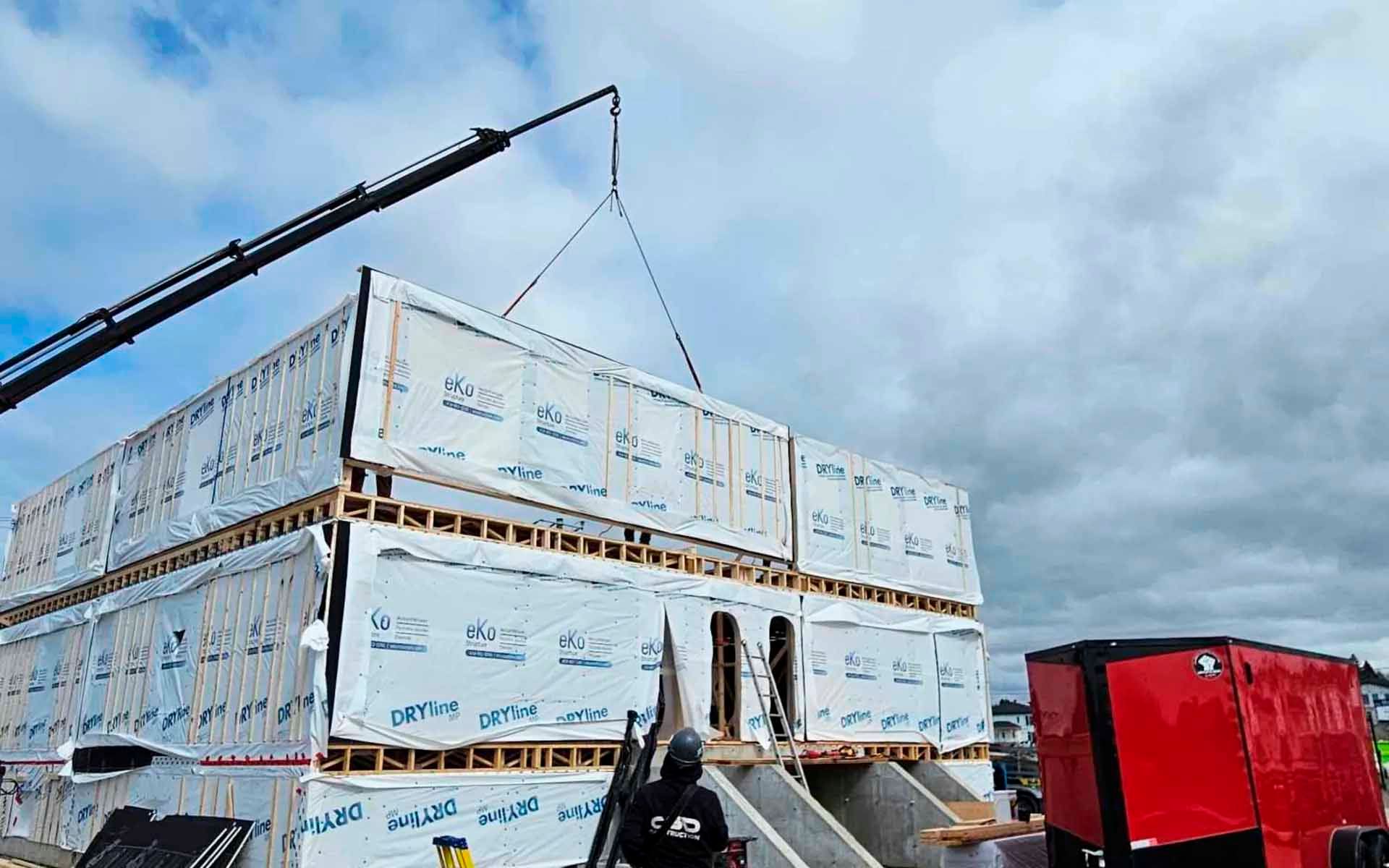 Grue soulevant des éléments de construction modulaires sur un chantier de construction sous un ciel nuageux.
