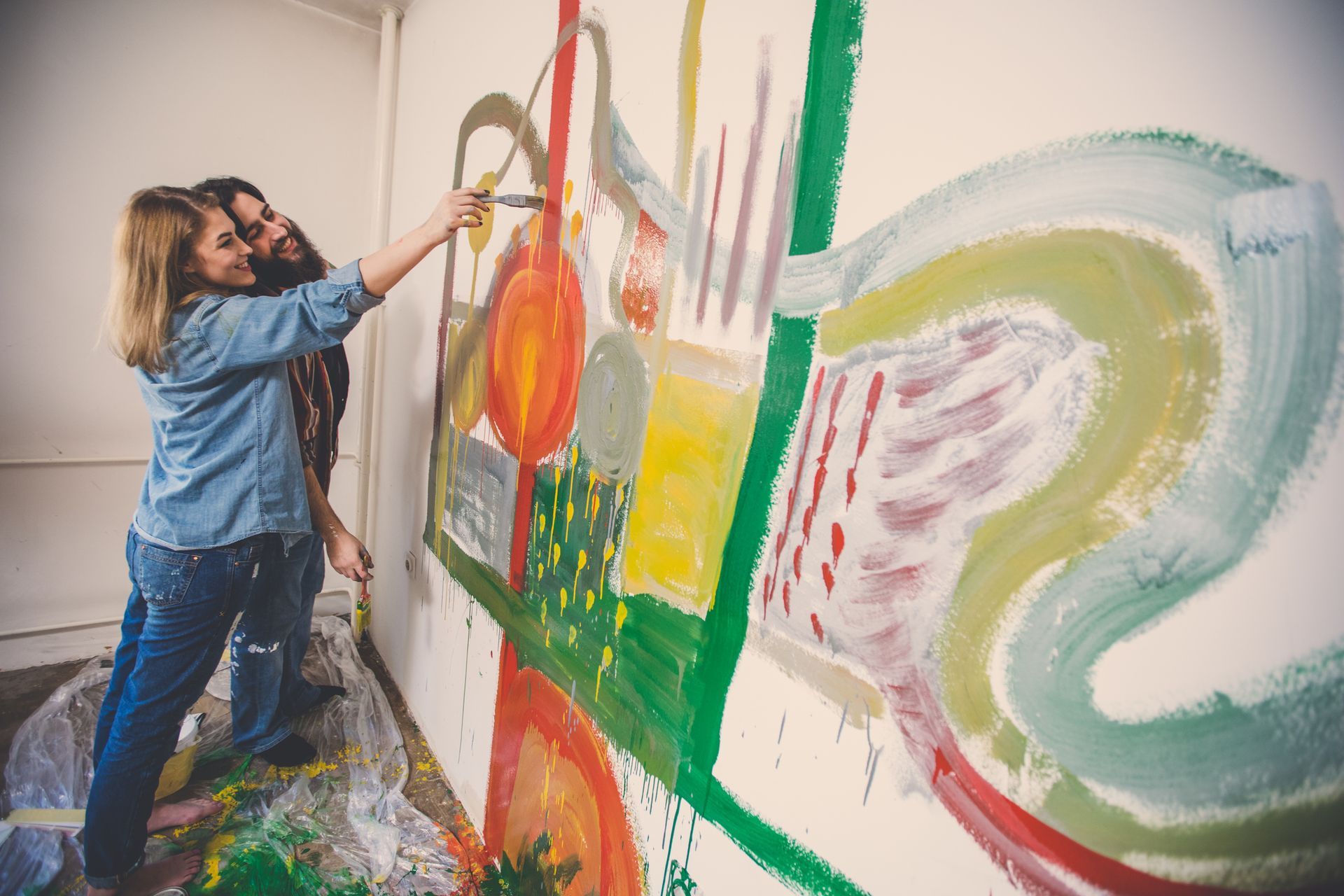 Two women are painting a picture on a wall in an art studio.