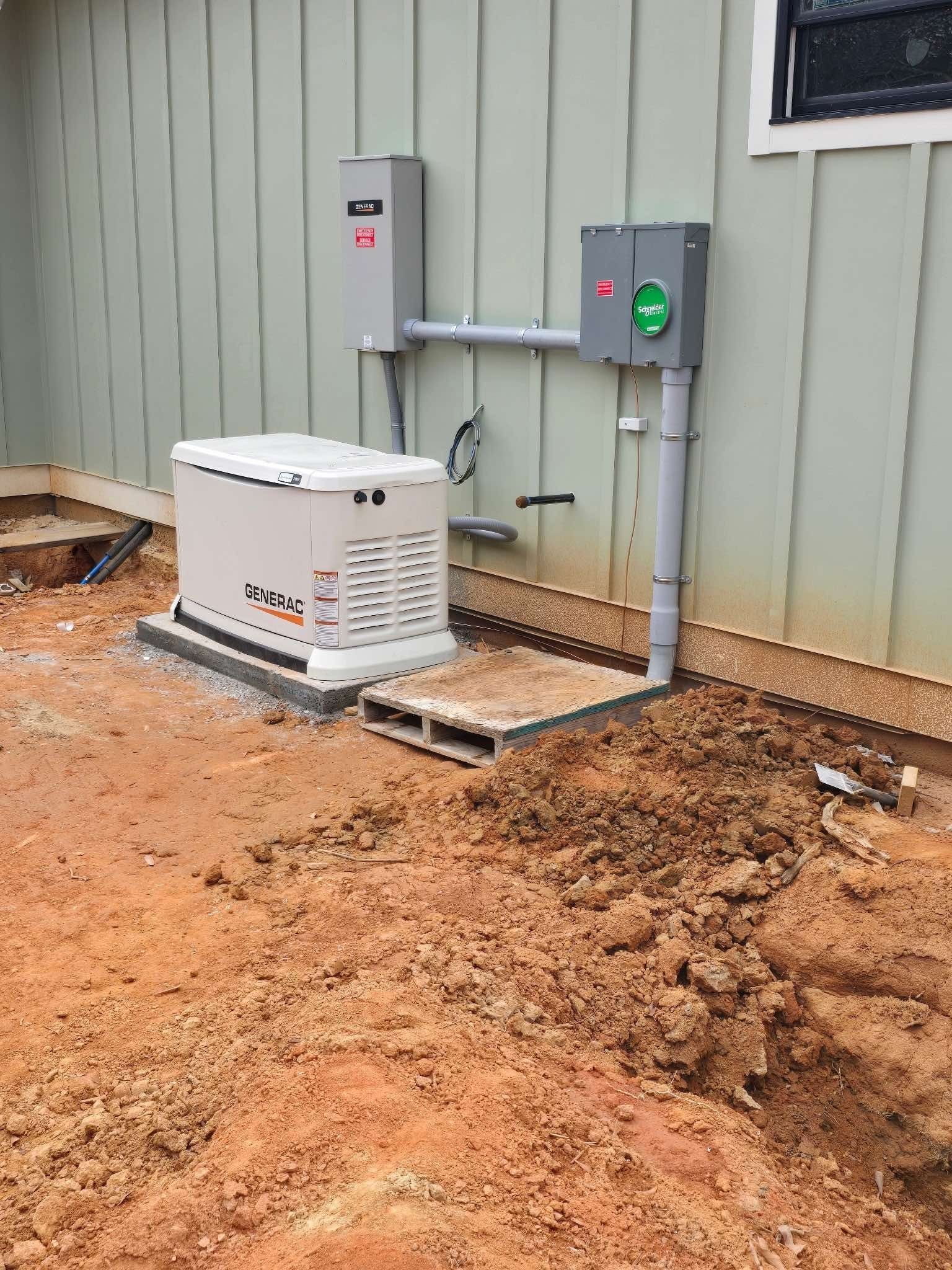 Generator and electrical components mounted on a wall; generator sits on a concrete pad near dirt.