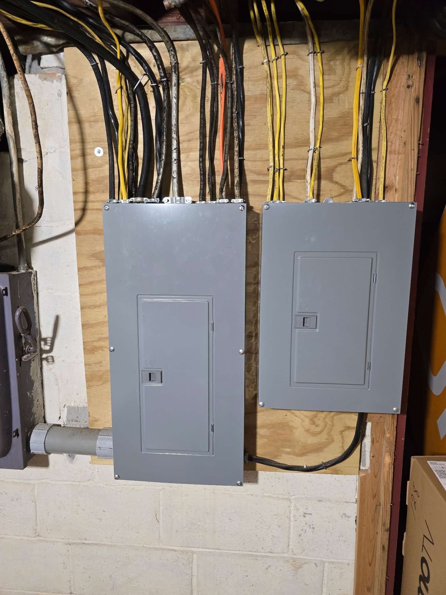 Two gray electrical panels mounted on wood with bundled wires above.