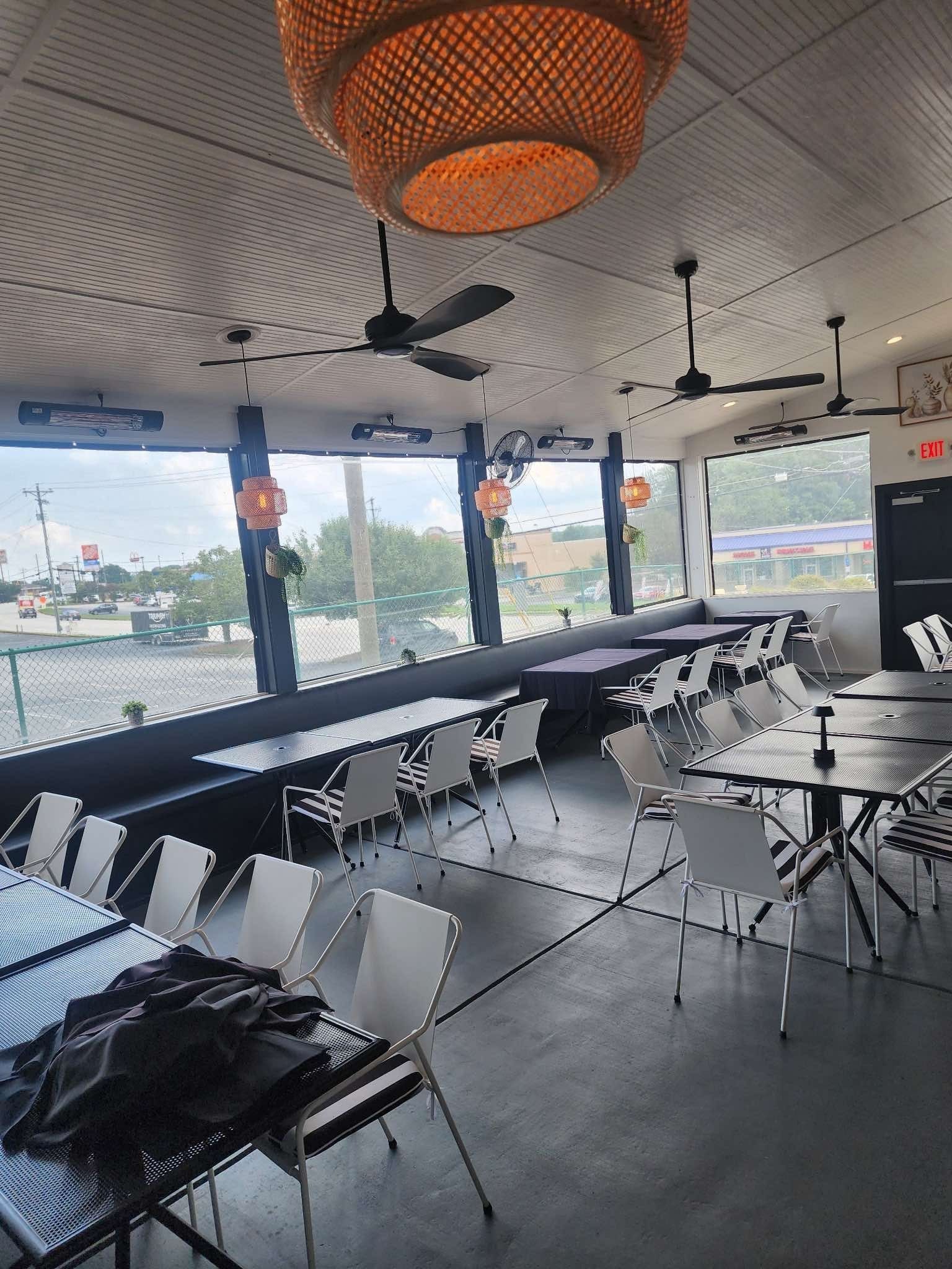 Interior view of a modern restaurant with tables, chairs, large windows, and decorative lighting.