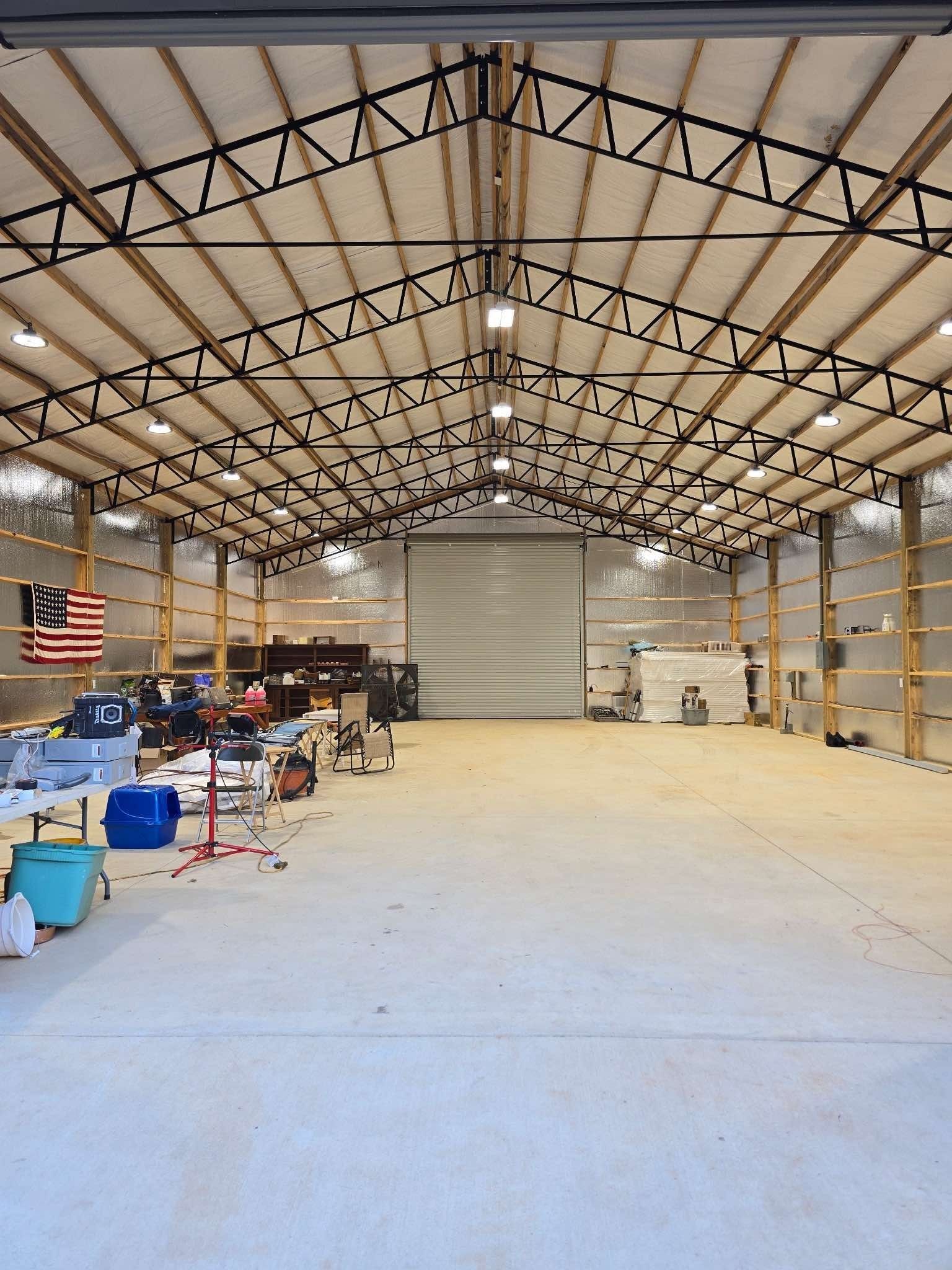Large, empty workshop; overhead lighting, metal trusses; American flag on the left, garage door in the center.