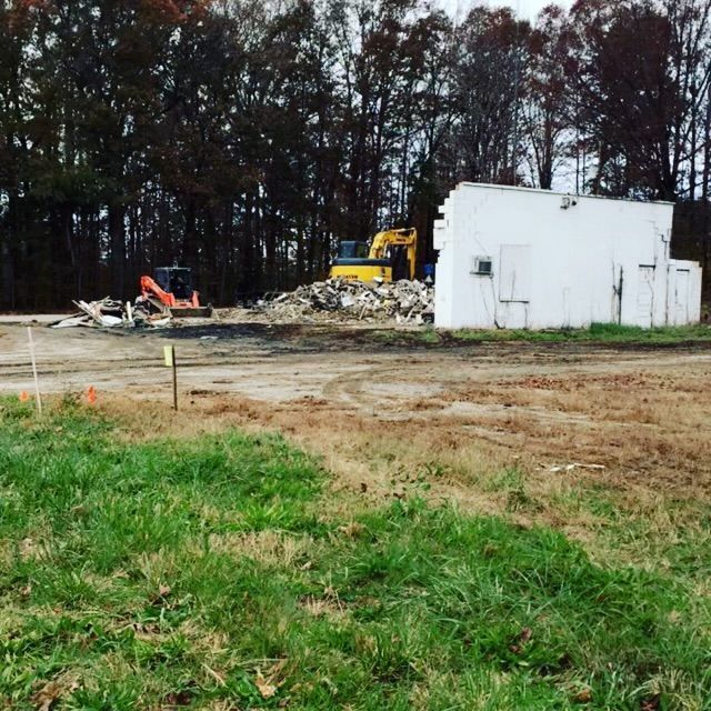 A white building is being demolished with a yellow excavator in the background
