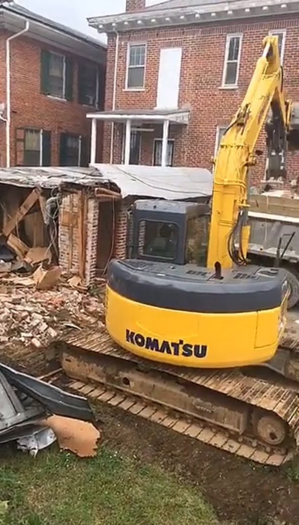 A yellow komatsu excavator is demolishing a brick house.