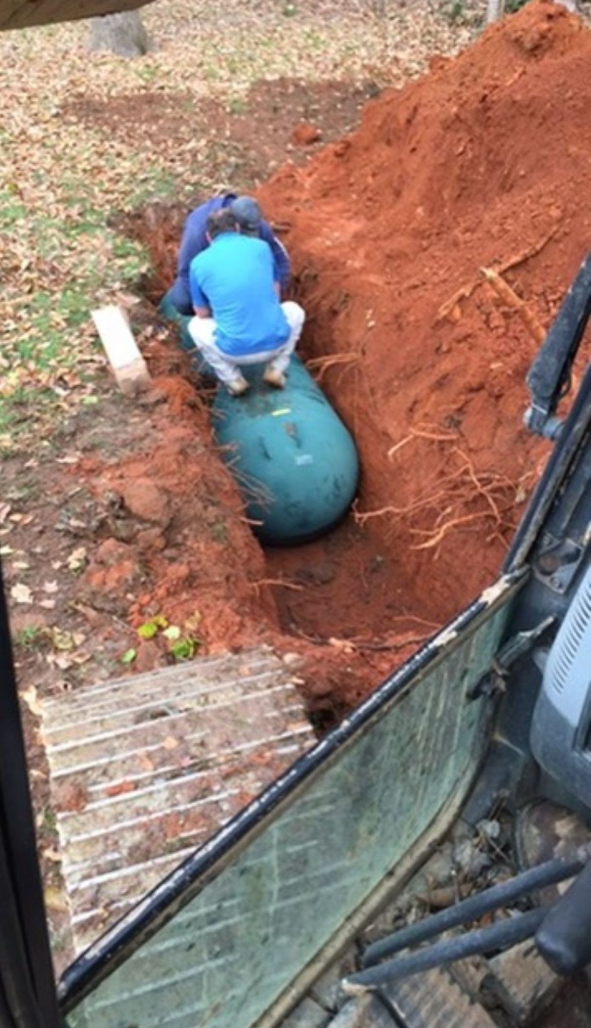 A man is sitting on top of a green bag in the dirt.