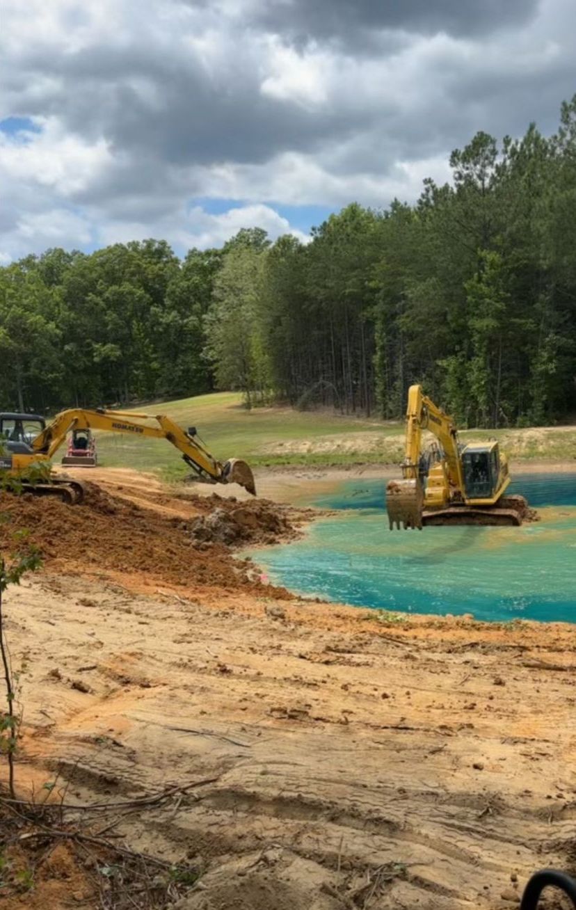 A couple of excavators are working on a pond.