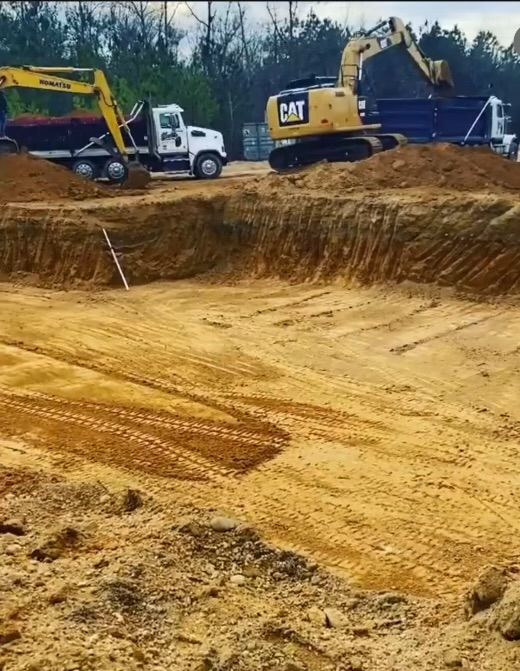 A cat excavator is digging a hole in a dirt field.