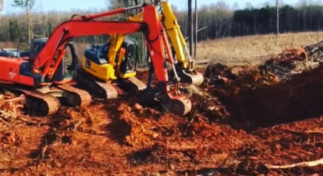 A group of excavators are digging a hole in the dirt.