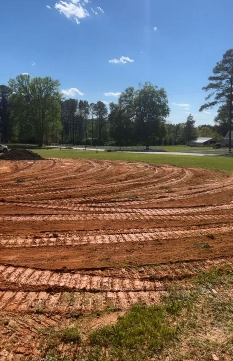 A dirt field with tractor tracks in it and trees in the background.