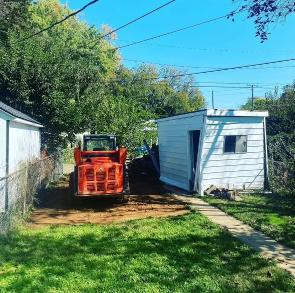 A red tractor is parked in front of a white shed.