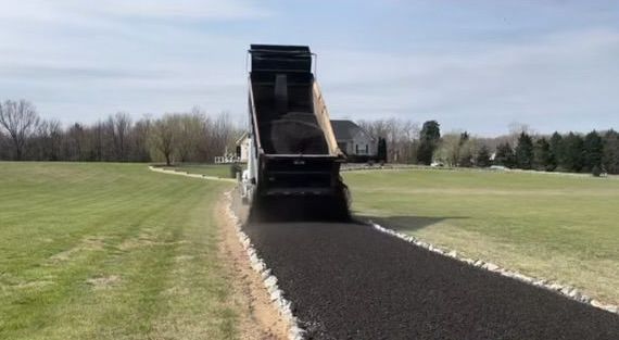 A dump truck is driving down a road next to a field.