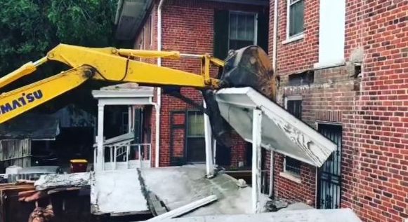A yellow komatsu excavator is digging into a brick building.