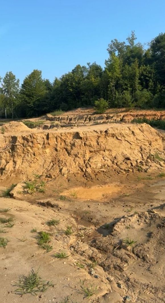 A large pile of dirt and rocks in a field with trees in the background.