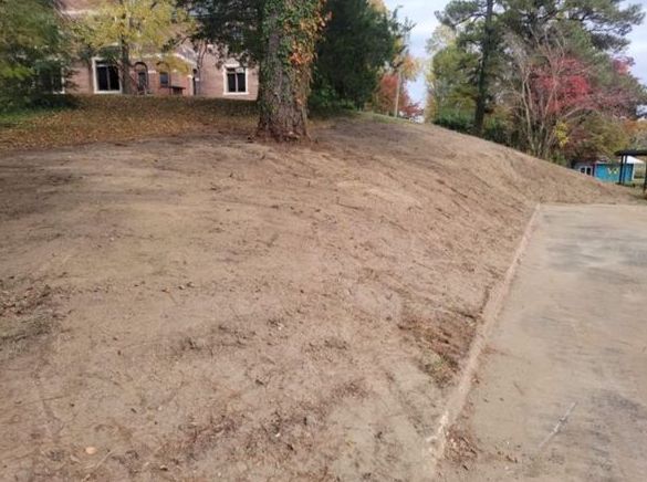 A dirt hill with a concrete curb and a house in the background.