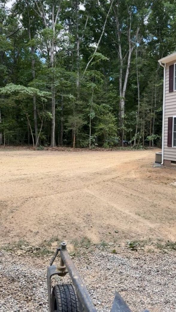 A trailer is parked in a dirt lot in front of a house.