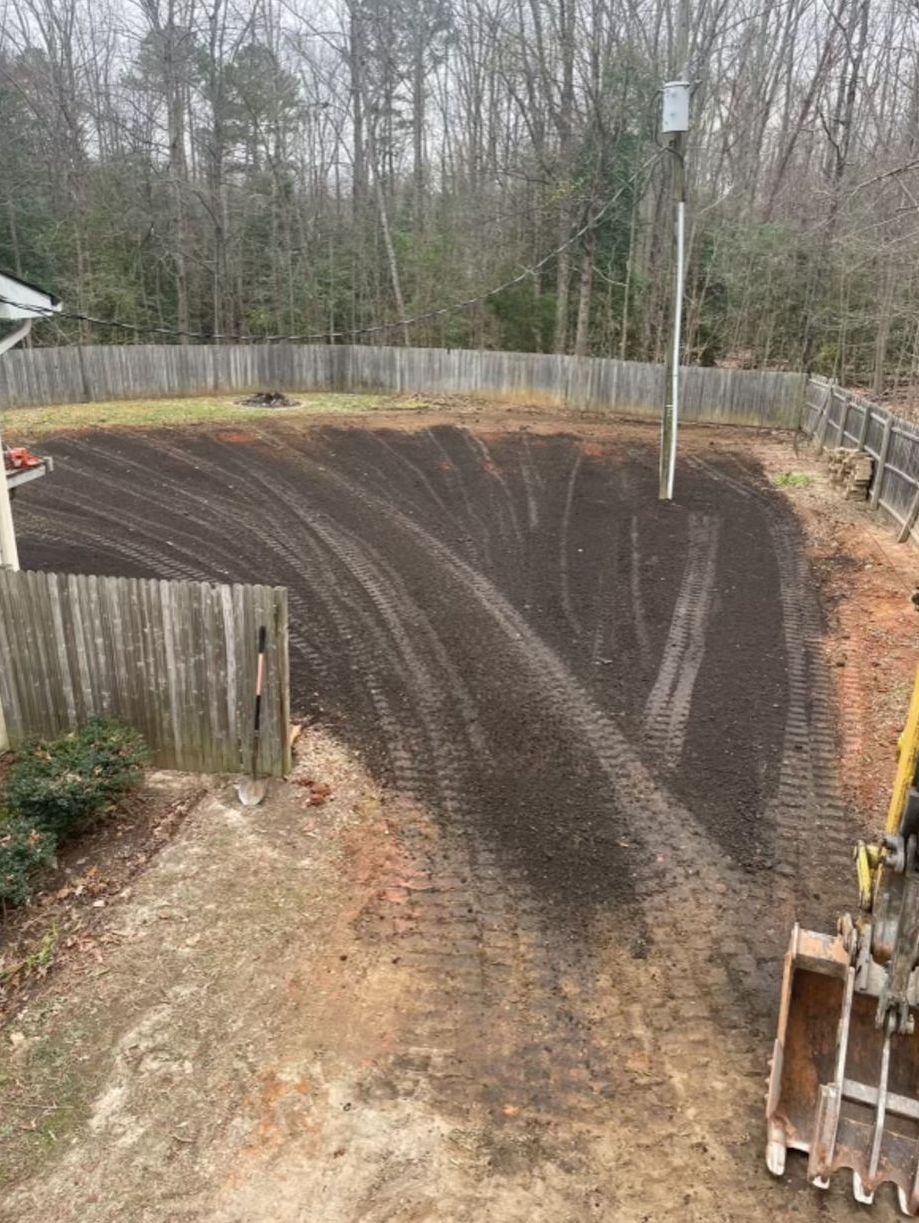 A large dirt field in a backyard with a fence and trees in the background.