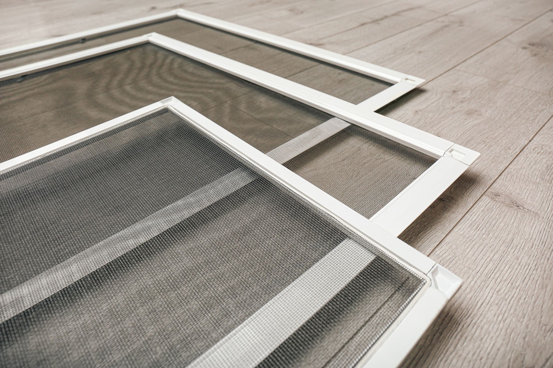 Three mosquito screens are stacked on top of each other on a wooden floor.