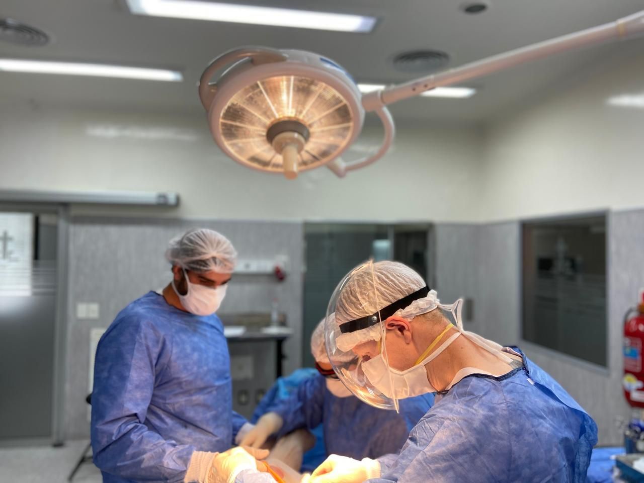 Cirujanos con uniformes azules realizan cirugías bajo las brillantes luces del quirófano.