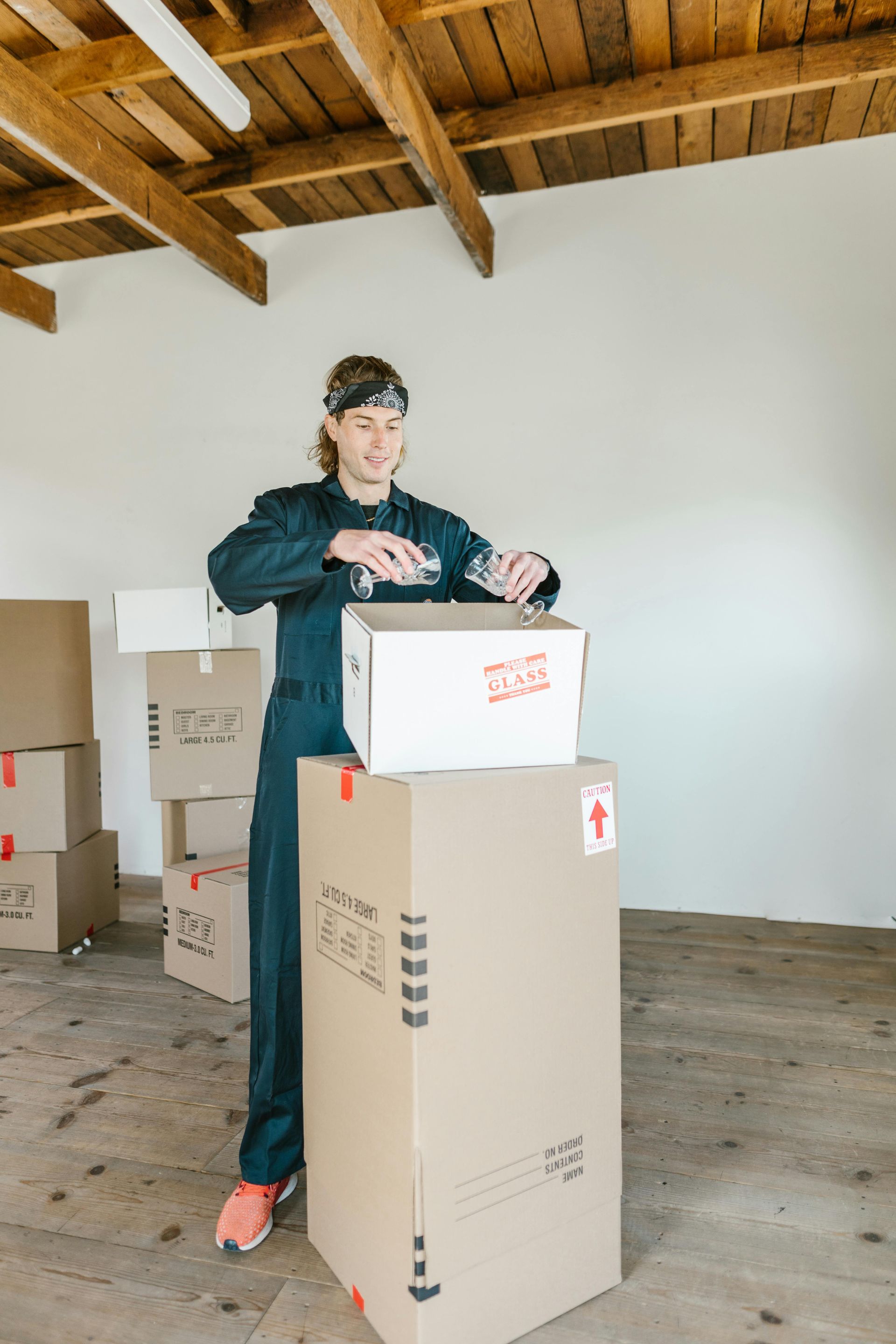 Person in blue jumpsuit packing a box in a room with other boxes.